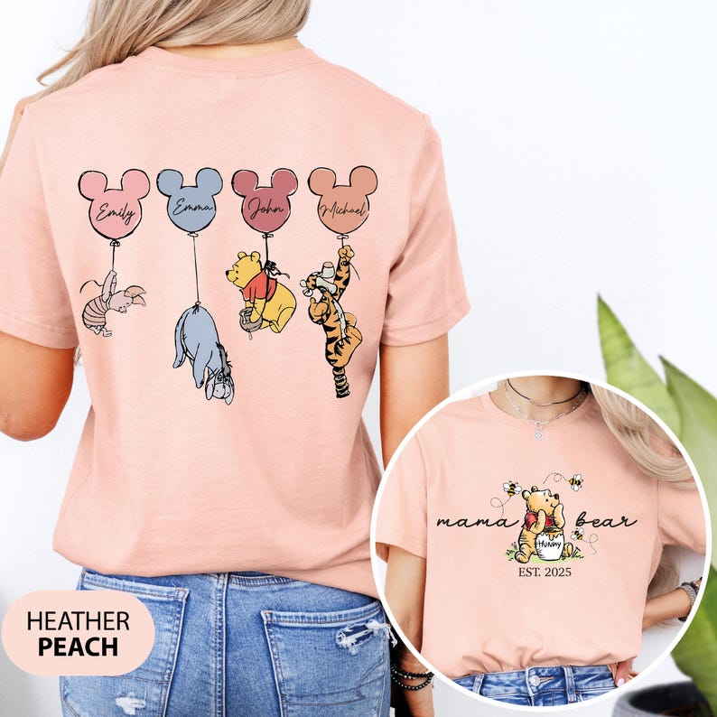 May include: A heather peach t-shirt with a Winnie the Pooh theme. The back of the shirt features four characters from Winnie the Pooh holding onto balloons with names written on them. The front of the shirt features Winnie the Pooh holding a jar of honey with the text "mama bear est. 2025".