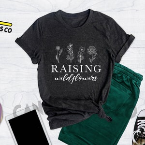 K&ouml;nnte beinhalten: Heather dunkelgraues T-Shirt mit einer wei&szlig;en Grafik von Blumen und dem Text "Raising wildflowers".