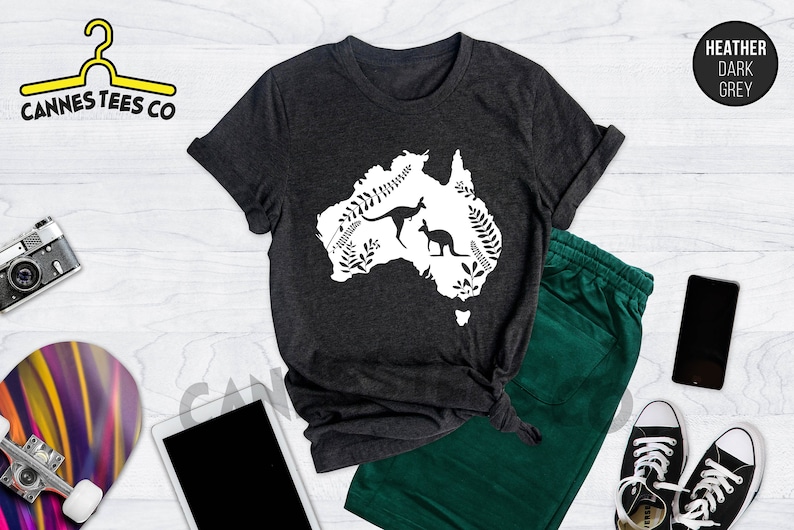 Może przedstawiać: Szary t-shirt w kolorze ciemnego melanżu z białym nadrukiem przedstawiającym zarys Australii z dwoma kangurami w środku. Nadruk jest otoczony białymi wzorami kwiatowymi.