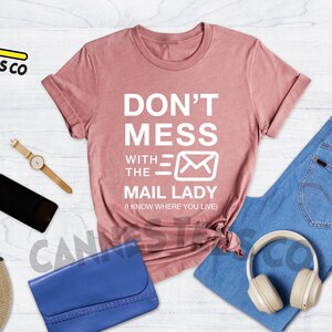 May include: A heather mauve t-shirt with the text "Don't Mess With The Mail Lady (I Know Where You Live)" in white.