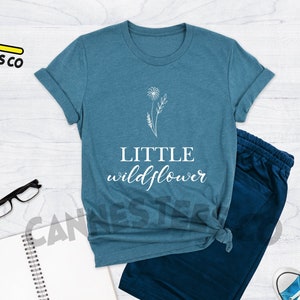 K&ouml;nnte beinhalten: Ein blaues T-Shirt mit einem wei&szlig;en Umriss einer Blume und dem Text "LITTLE wildflower".