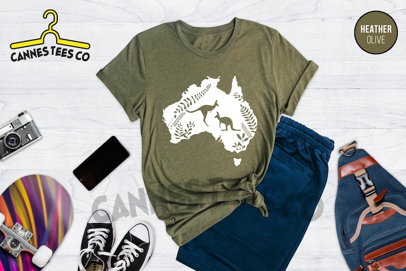 Może przedstawiać: Zielona koszulka z białym obrysem kontynentu Australii z dwoma kangurami w środku. Tekst "Cannes Tees Co" znajduje się w lewym g&oacute;rnym rogu obrazu. Tekst "Heather Olive" znajduje się w prawym g&oacute;rnym rogu obrazu.