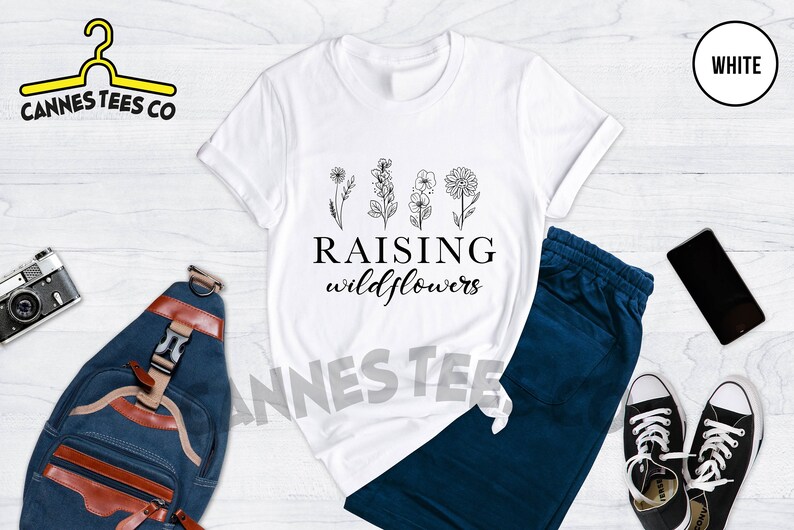 K&ouml;nnte beinhalten: Wei&szlig;es T-Shirt mit einer schwarzen Grafik von Blumen und dem Text "Raising wildflowers".
