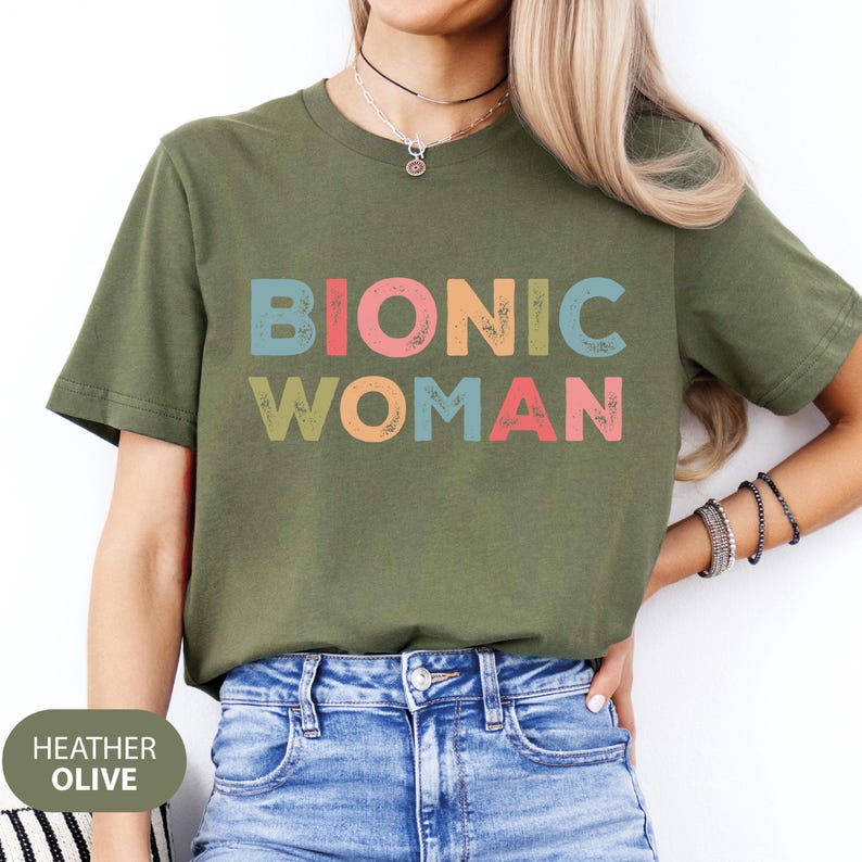 May include: A green t-shirt with the text "Bionic Woman" in colorful, distressed letters. The shirt is made of a soft, comfortable material and has a relaxed fit.