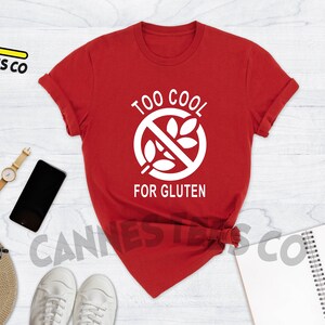 May include: Red t-shirt with a white graphic that says "Too Cool For Gluten" and a white gluten-free symbol.