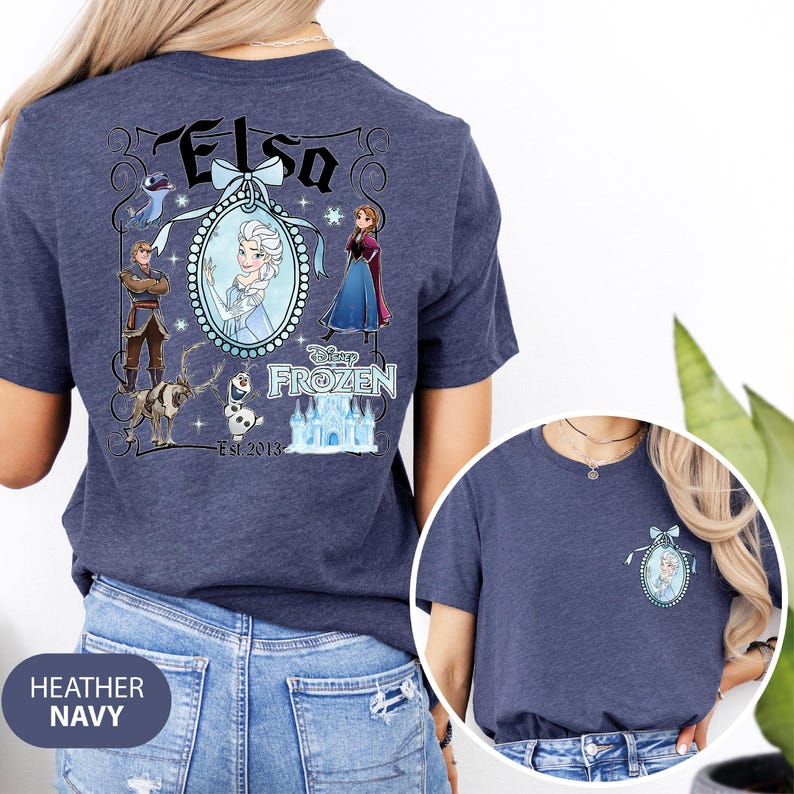 May include: Heather navy blue t-shirt featuring a graphic of Elsa from Disney's Frozen. The design includes Elsa's name, characters, and the text "Disney Frozen Est. 2013". The shirt has a crew neck and short sleeves.