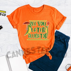 May include: Orange t-shirt with a green alligator graphic and the text "See you later alligator".