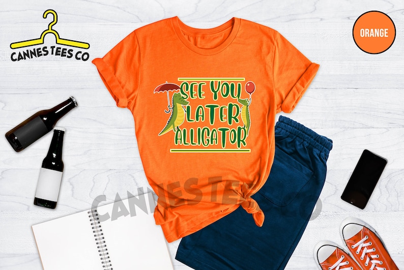 May include: Orange t-shirt with a green alligator graphic and the text "See you later alligator".