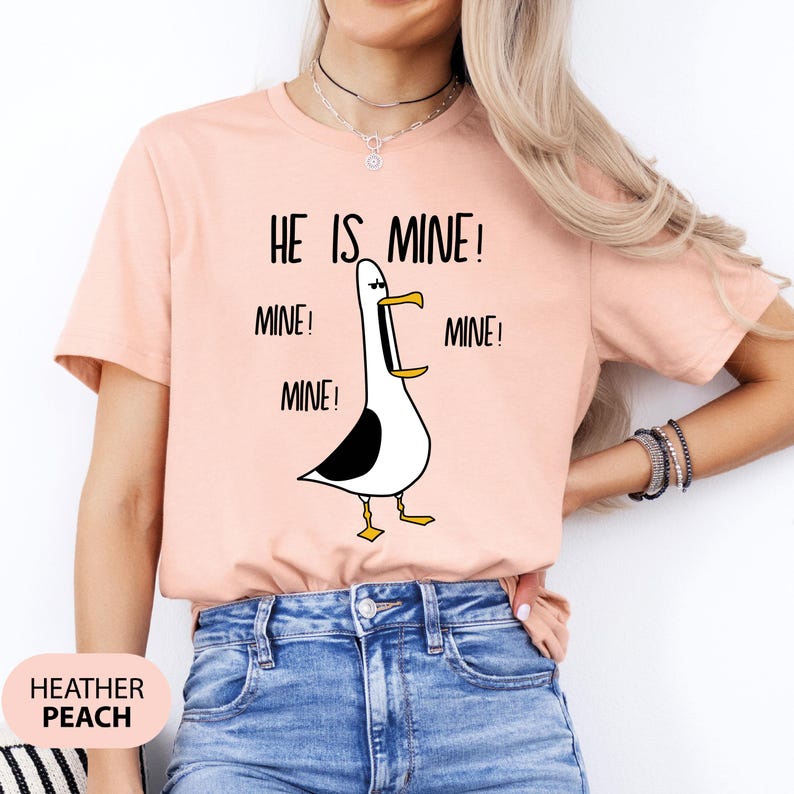 May include: A pink t-shirt with a cartoon seagull and the text "He is mine! Mine! Mine! Mine!" printed on it.