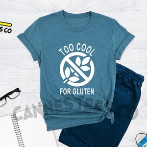 May include: A teal blue t-shirt with a white graphic of a crossed-out wheat stalk and the text "Too Cool For Gluten".