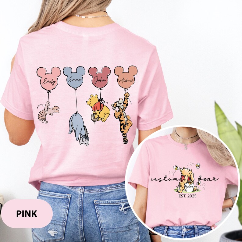 May include: Pink t-shirt with a Winnie the Pooh design featuring four characters holding balloons with names on them. The text "costume bear est. 2025" is on the bottom of the shirt.