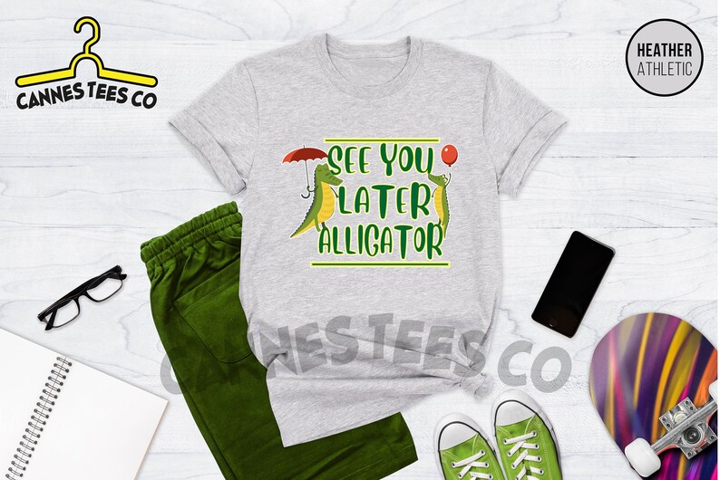 May include: A heather grey t-shirt with a green alligator holding an umbrella and another green alligator holding a red balloon. The text on the shirt says "See You Later Alligator".