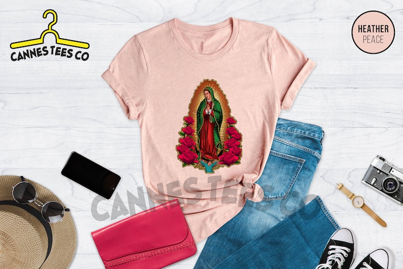 May include: A pink t-shirt with a graphic of Our Lady of Guadalupe surrounded by red roses. The text "HEATHER PEACE" is in the upper right corner of the image.