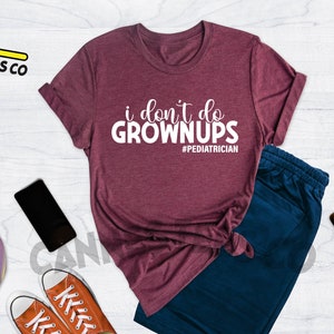 May include: Heather maroon t-shirt with the text "i don't do grown ups #pediatrician".