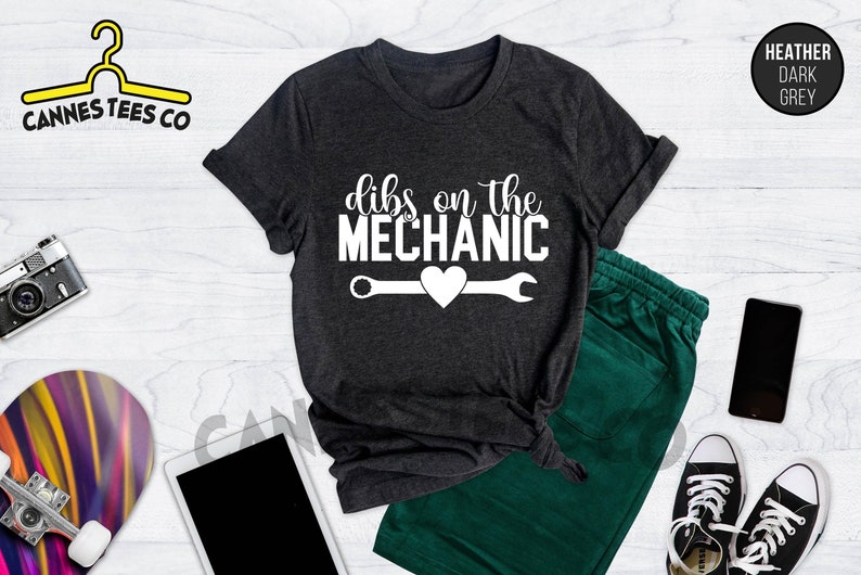 Może przedstawiać: Szary t-shirt w kolorze ciemnego melanżu z napisem "dibs on the mechanic" w białym kolorze. Pod napisem znajduje się biały klucz z sercem w środku.