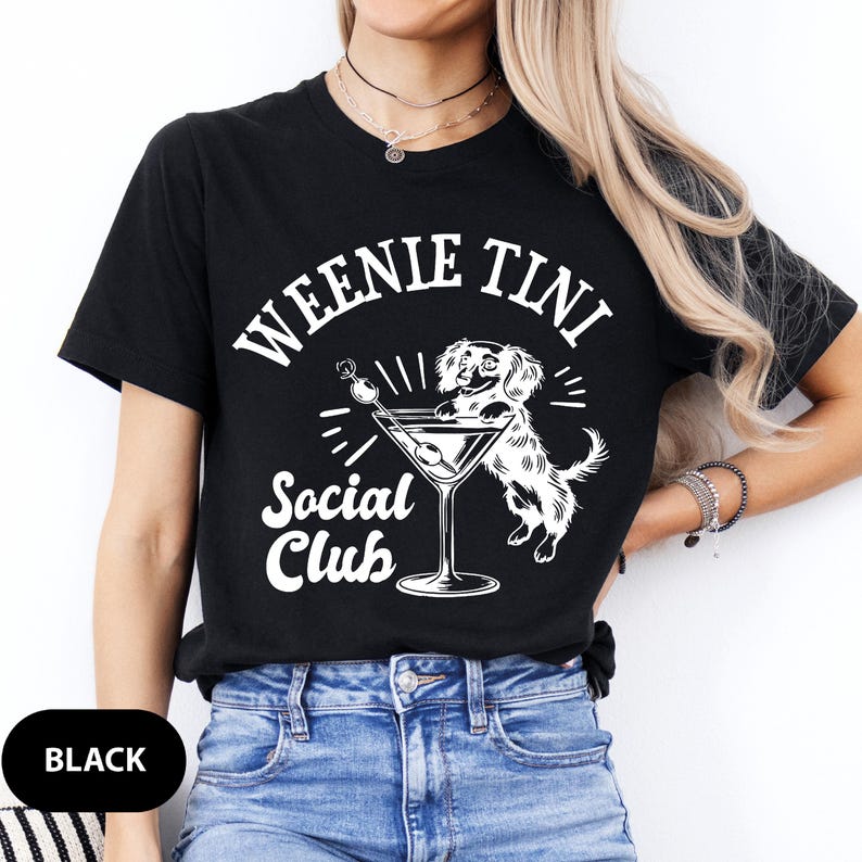 May include: Black t-shirt with white text that reads "Weenie Tini Social Club". A cartoon dachshund is holding a martini glass with an olive.