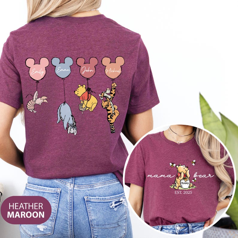 May include: Heather maroon t-shirt with a design of Winnie the Pooh and friends on balloons. The back of the shirt has the names "Emily", "Emma", "John", and "Michael" on the balloons. The front of the shirt has the text "mama bear est. 2025" with a Winnie the Pooh illustration.