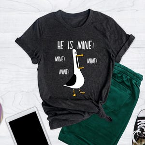 May include: A dark heather grey t-shirt with a white graphic of a seagull with the text "He is mine! Mine! Mine! Mine!"