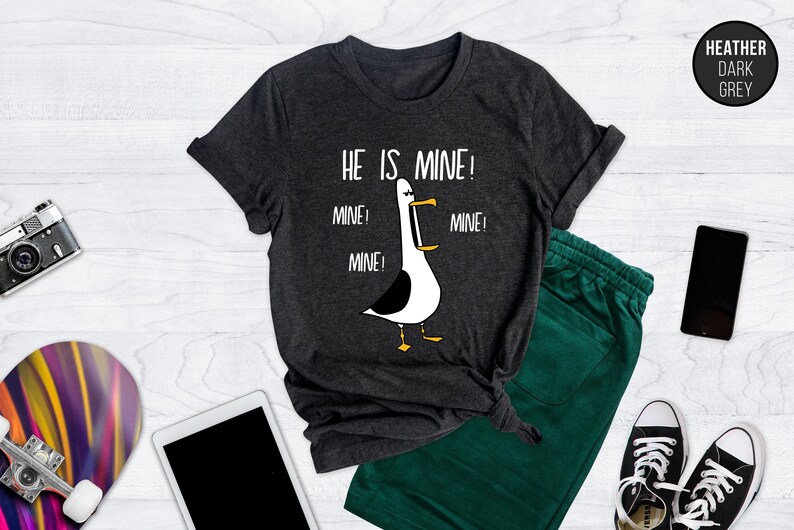 May include: A dark heather grey t-shirt with a white graphic of a seagull with the text "He is mine! Mine! Mine! Mine!"