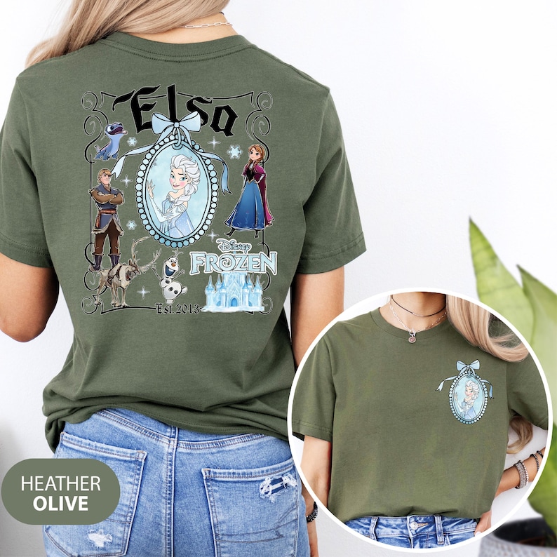 May include: Heather olive green t-shirt featuring a Disney Frozen design. The back of the shirt displays the name "Elsa" in a decorative frame with character illustrations. The front of the shirt has a smaller version of the Elsa design.