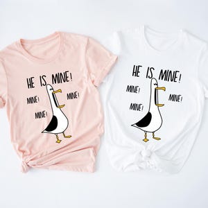 May include: Two t-shirts with a cartoon seagull graphic and the text "He is mine!" repeated multiple times. The shirts are pink and white.