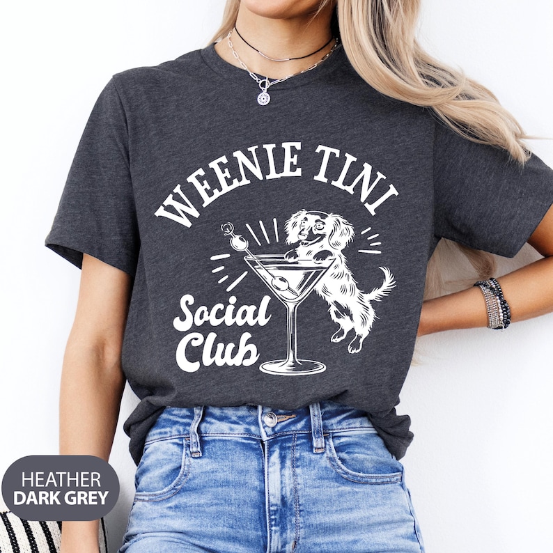 May include: Heather dark grey t-shirt with a white graphic of a dachshund dog holding a martini glass. The text "Weenie Tini Social Club" is printed on the shirt.