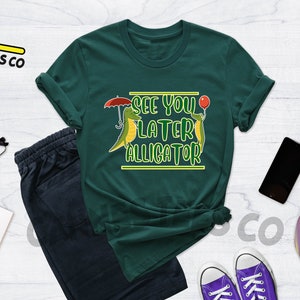 May include: A green t-shirt with a graphic of two cartoon alligators. The text on the shirt reads "See you later alligator".
