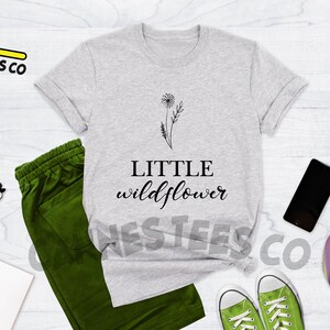 K&ouml;nnte beinhalten: Ein hellgraues T-Shirt mit einem schwarzen Motiv eines L&ouml;wenzahns und dem Text "LITTLE wildflower".