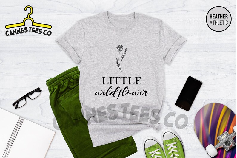 K&ouml;nnte beinhalten: Ein hellgraues T-Shirt mit einem schwarzen Motiv eines L&ouml;wenzahns und dem Text "LITTLE wildflower".
