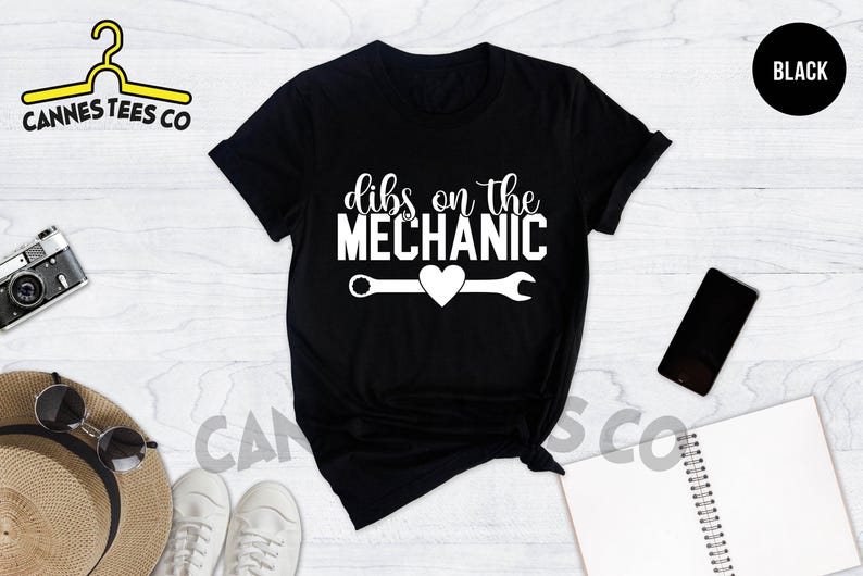 Może przedstawiać: Czarny T-shirt z białym napisem "Dibs on the Mechanic" z grafiką klucza i serca.