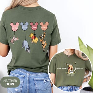 May include: A green t-shirt with a Winnie the Pooh theme. The back of the shirt features five cartoon characters holding balloons with names on them. The front of the shirt has the text "mama bear est. 2025".