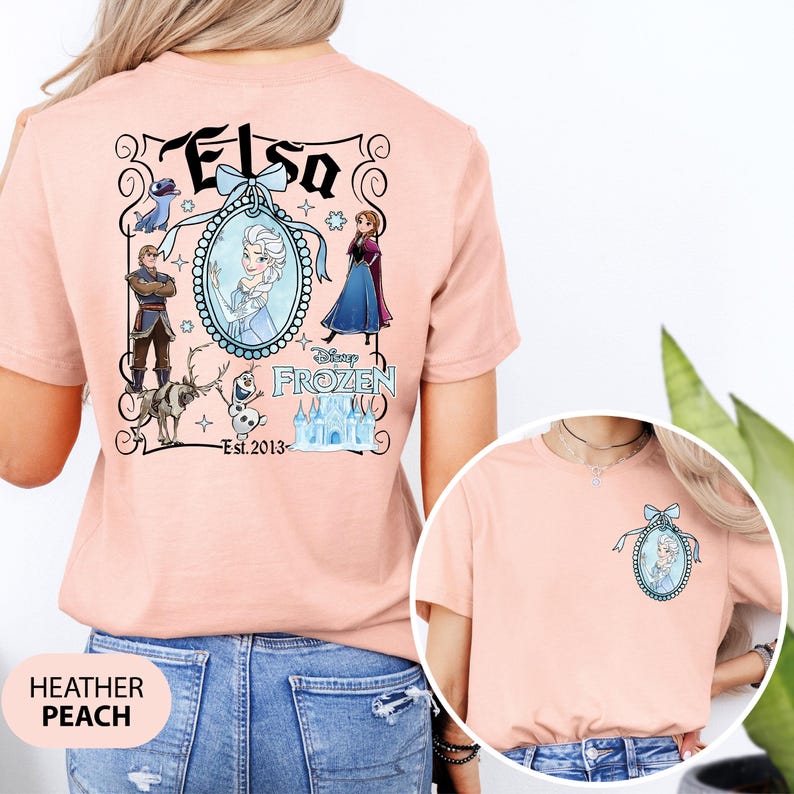 May include: Heather peach t-shirt featuring a Disney Frozen design. The back of the shirt displays the word "Elsa" above an oval portrait of Elsa, surrounded by other characters and the text "Est. 2013". A smaller version of the design is on the front.