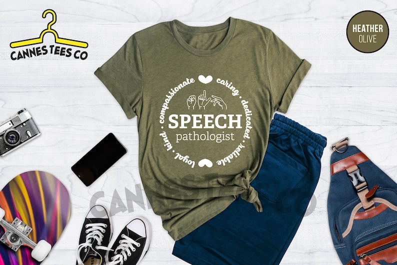 Op de afbeelding: Een groen T-shirt met een wit cirkelvormig ontwerp met de tekst "SPEECH pathologist" met gebarentaal voor het woord "speech". De cirkel bevat ook de woorden "compassionate, caring, dedicated, reliable, loyal, kind" rond de buitenkant.