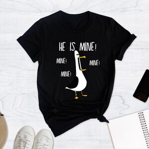 May include: Black t-shirt with a white graphic of a seagull with the text "He is mine! Mine! Mine! Mine!"