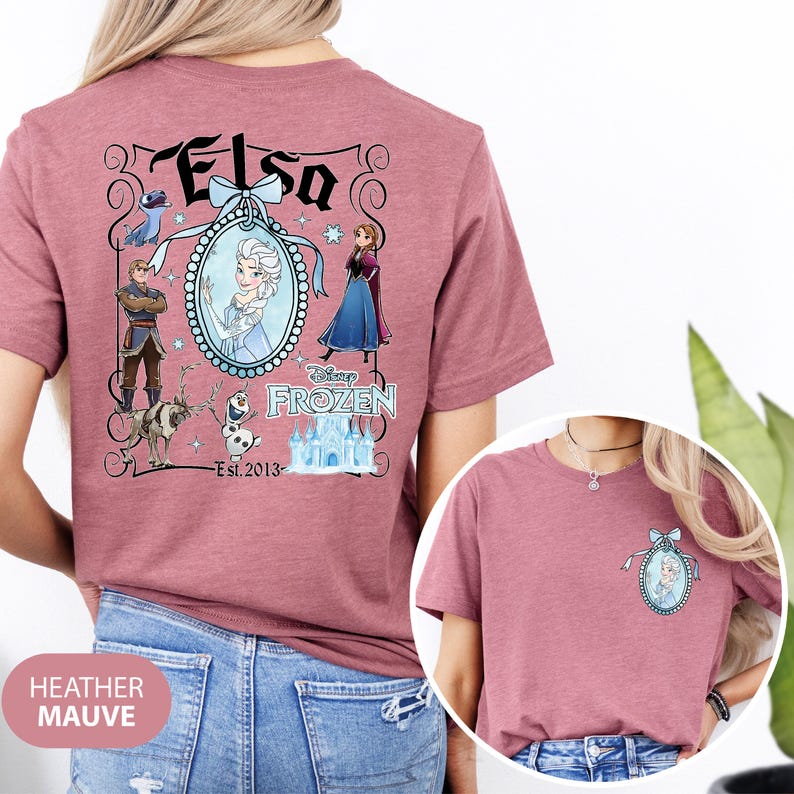 May include: Heather mauve t-shirt featuring a graphic of Elsa from Disney's Frozen. The design includes Elsa's image, other characters, and the text "Elsa" and "Frozen". The shirt also has the text "Est. 2013".