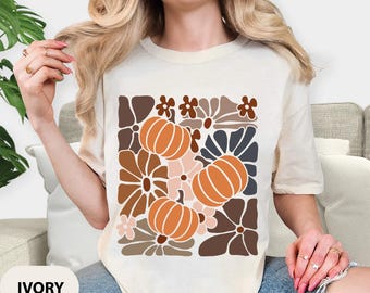 May include: Ivory-colored t-shirt featuring a retro floral and pumpkin design in shades of brown, orange, and cream. The graphic is centered on the front of the shirt. The word "IVORY" is printed at the bottom.