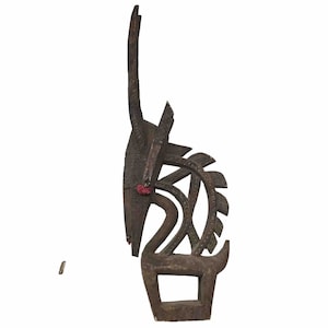 Puede incluir: Una escultura de madera marrón oscuro de un antílope con un cuerno largo y curvo. La escultura está tallada con intrincados detalles y tiene acentos rojos alrededor de los ojos.