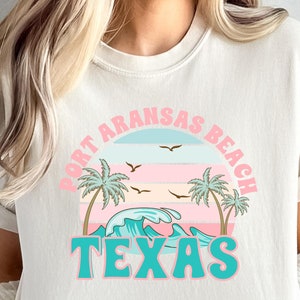 May include: A white t-shirt with a graphic design of a sunset over the ocean with palm trees and the text "Fort Aransas Beach Texas".