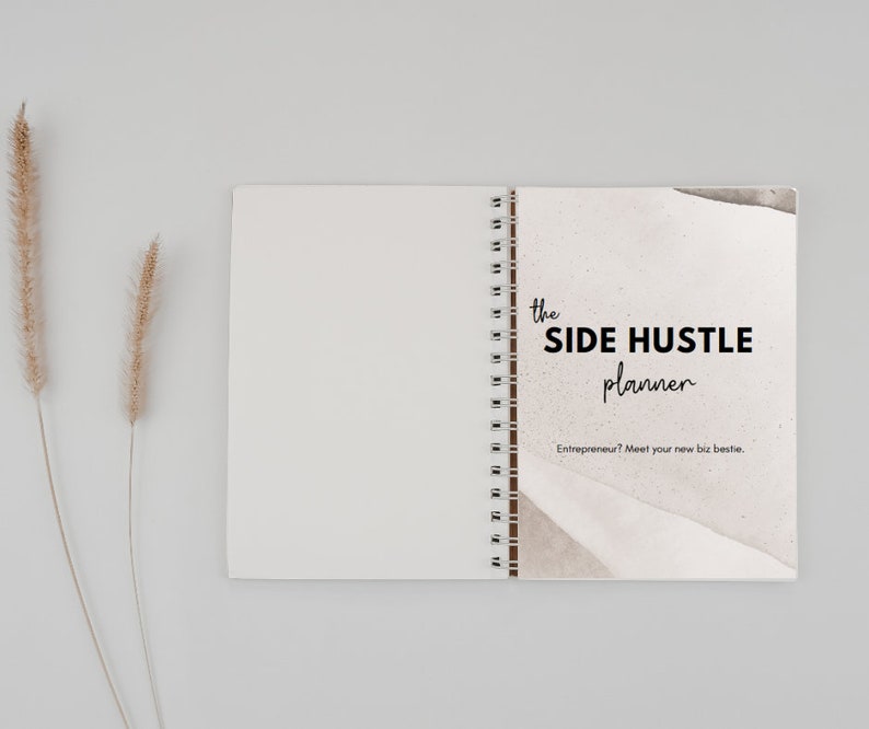 May include: A closed spiral bound notebook with a white cover and a brown and white abstract design on the front. The text "the SIDE HUSTLE planner" is printed in black on the front cover. The text "Entrepreneur? Meet your new biz bestie." is printed in black below the title.