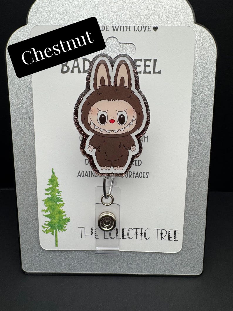Puede incluir: Un carrete de insignia con una criatura marr&oacute;n de dibujos animados con orejas de conejo y una sonrisa amenazante. El carrete de la insignia est&aacute; etiquetado "Chestnut" e incluye el texto "THE ECLECTIC TREE". El fondo incluye un gr&aacute;fico de &aacute;rbol verde.