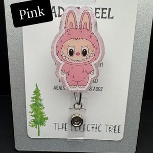 Puede incluir: Un portatarjetas rosa con un personaje de dibujos animados con un traje de conejito rosa y un borde brillante. El portatarjetas est&aacute; en una tarjeta blanca con la palabra "Pink" y el texto "The Eclectic Tree".
