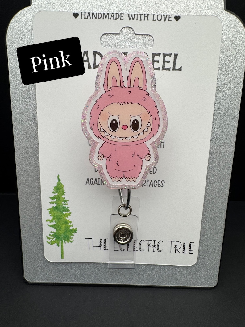 Puede incluir: Un portatarjetas rosa con un personaje de dibujos animados con un traje de conejito rosa y un borde brillante. El portatarjetas est&aacute; en una tarjeta blanca con la palabra "Pink" y el texto "The Eclectic Tree".