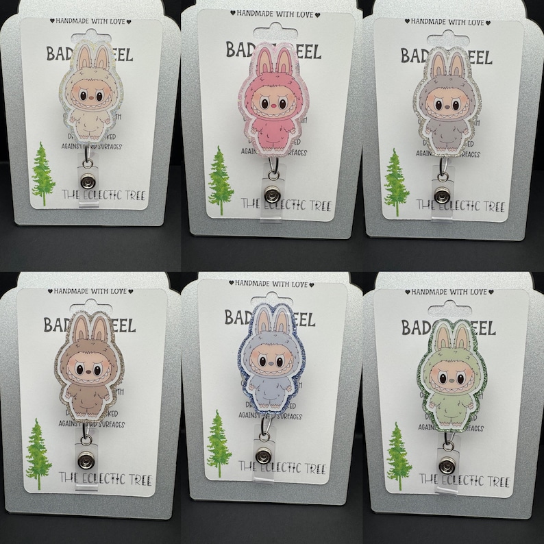 Puede incluir: Seis carretes para insignias con un personaje de conejo de dibujos animados en varios colores, incluyendo rosa, gris y azul. Cada carrete tiene un cord&oacute;n retr&aacute;ctil y un clip met&aacute;lico. Las tarjetas detr&aacute;s dicen "BAD EEL" y "THE ECLECTIC TREE."
