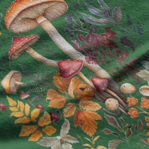 May include: A close-up of a green fabric with a watercolor illustration of mushrooms, leaves, and berries. The mushrooms have red and brown caps with white spots. The leaves are yellow, orange, and brown.