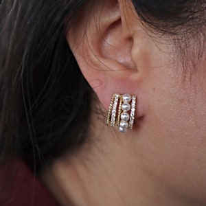 May include: Gold hoop earrings with a row of pearls and small clear stones.