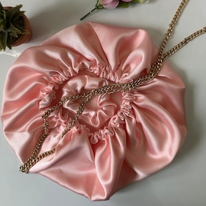 May include: A pink satin sleep cap with a gold chain attached. The cap is gathered at the top and has a smooth, silky texture.