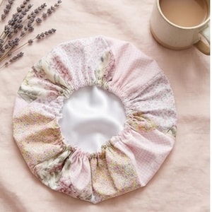 Könnte beinhalten: Eine Duschhaube mit floralem Muster und weißem Satin-Innenfutter. Die Haube hat ein Patchwork-Design mit rosa, weißen und grünen Blumen- und Vichy-Mustern. Die Haube ist kreisförmig und am elastischen Rand gerafft.