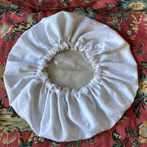 Peut inclure: Une charlotte de douche en coton blanc avec un bord élastique plissé et un motif floral délicat.