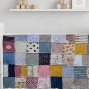 Pode incluir: Uma colcha de retalhos com uma grade de peças de tecido quadradas em várias cores e padrões, incluindo amarelo mostarda, azul claro, rosa e cinza, juntamente com estampas de estrelas pretas, motivos florais e listras, sobre um berço branco.