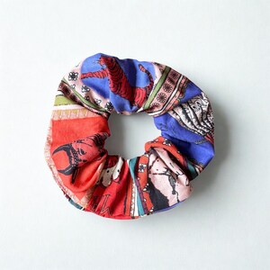 May include: A colorful scrunchie with a vibrant pattern. The fabric features a red tiger on a blue background, along with other patterns in red, green, and white. The scrunchie is designed to hold hair in place.